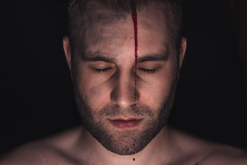 Portrait of man with blood on his face on dark background.