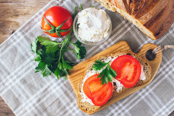 Sandwich of crispy bread, fresh tomatoes, cream cheese with herbs