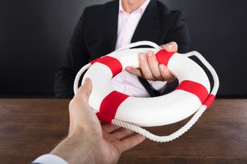 Businessman Passing A Lifebuoy To A Partner