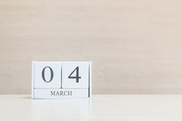 Closeup surface white wooden calendar with black 4 march word on blurred brown wood desk and wood wall textured background with copy space , selective focus at the calendar