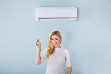 Woman Holding Remote Controller Of Air Conditioner - obrazy, fototapety, plakaty