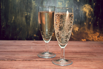 wine glasses with white sparkling wine on a wooden table against black and gold wall