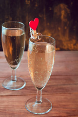 wine glasses with white sparkling wine and golden wedding rings on a wooden table against black and gold wall