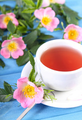 Cup of tea and wild rose flower on blue boards