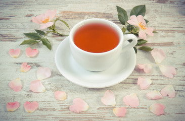 Vintage photo, Cup of tea and wild rose flower on old rustic wooden background