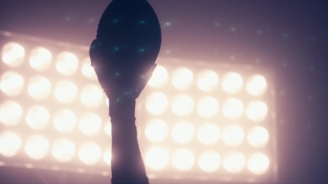 CU Silhouette of male American football player rising a ball in his hand against bright stadium illumination lights. 4K UHD RAW edited footage