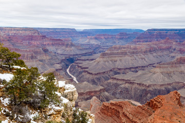 Winter view of the Grand Canyon from the South Rim looking west. Snow adorns the rocky outcrop of the nearby cliff; the Colorado River far below is muddy from the recent storm.
