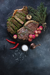 Whole and sliced bbq striploin steaks with roasted radish and chimichurri, above view with copyspace