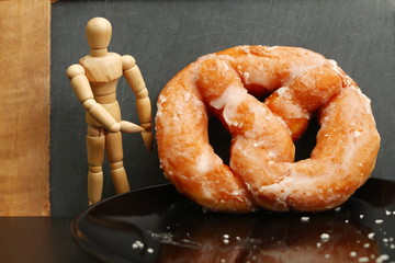 The pretzel shaped sugar donut with artist wood doll represent the donut recipe and bakery concept related idea.