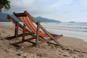 End of leisure season on sea beach of tropical country. Rain season in Thailand. Couple of deck chairs on seacoast in cloudy weather