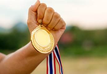 Fototapeta na wymiar hand raised and holding gold medal against white background, award concept
