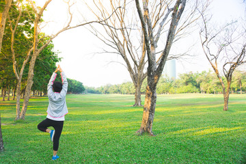 Woman doing yoga pose on the grass field in city park on sunny day 