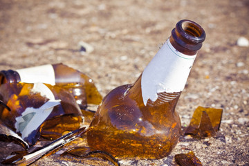 Shattered beer bottle resting on the ground: alcoholism concept - toned image with copy space