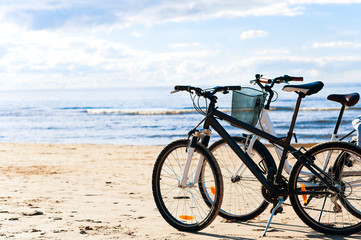 Fototapeta na wymiar Two bicycles standing on the beach sand on sea coastline