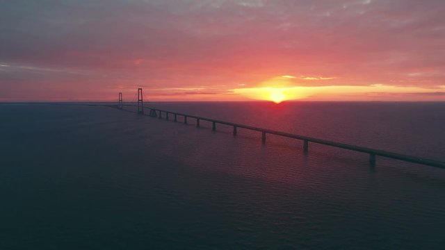 An aerial view of large Storebaelt bridge over sea in Denmark with sunset in background.