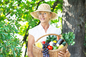 Woman wearing hat with fresh fruit and vegetables in the basket in her hands
