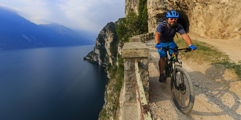 Mountain biking man at sunrise over Lake Garda on path Sentiero della Ponale, Riva del Garda, Italy