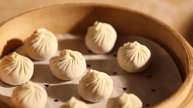 A cook is making dumplings with his hands and is placing them in a bowl. He uses a bamboo steamer basket to place it on a pot of boiling water