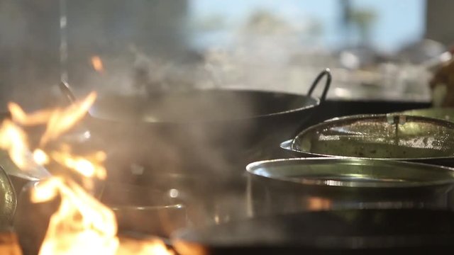 Several cooks are cooking in the kitchen of a restaurant. They are using a wok that is used to saute the food by means of a constant movement denominated in the Chinese gastronomy like Wok hei.