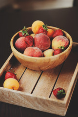 fresh summer fruits on wooden plate. Strawberries, peaches and apricots in rustic farm kitchen