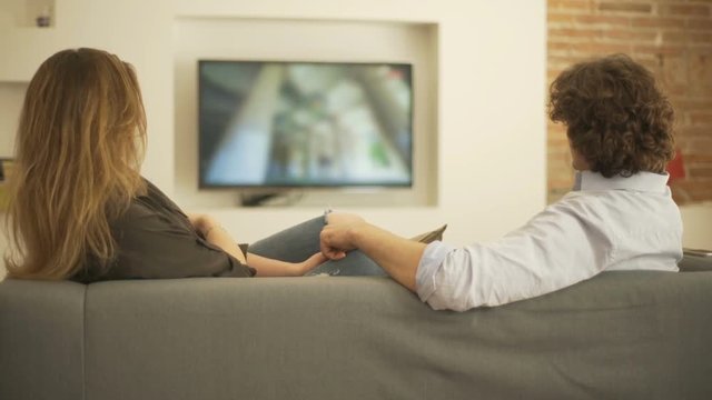 Couple sitting on the sofa and watching something on television
