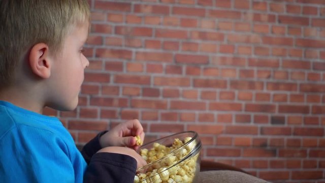 Little boy sitting with popcorn on sofa and watching cinema