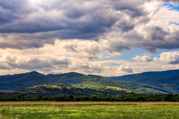 countryside summer landscape with field, forest and mountain ridge