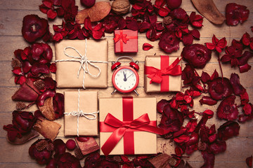 gifts of different sizes, alarm clock and romantic dried flower petals on the wonderful brown wooden background