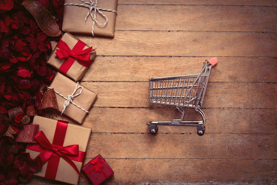 gifts of different sizes, shopping cart and romantic dried flower petals on the wonderful brown wooden background