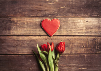 Obraz na płótnie Canvas heart shaped cookie and bunch of tulips lying on the wonderful brown wooden background
