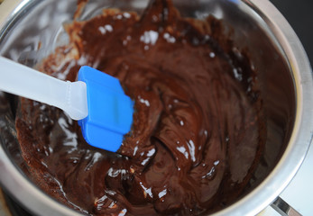 Chocolate and butter melt in a water bath. Blue silicone spatula. The process of making the dessert or sweets