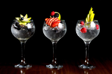 tall wine style glass three glasses of clear gin and tonic cocktail drink with fresh fruit garnish - obrazy, fototapety, plakaty