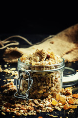 Baked muesli with raisins and sunflower seeds in a glass jar, black background, selective focus