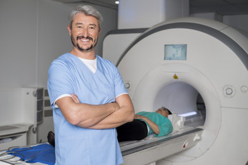 Doctor With Arms Crossed While Patient On CT Scan Machine