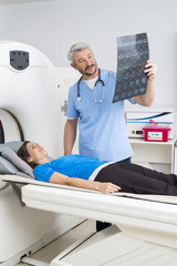 Fototapeta premium Doctor Explaining X-ray To Patient Lying On MRI Machine