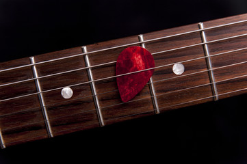 Red guitar pick on the fingerboard