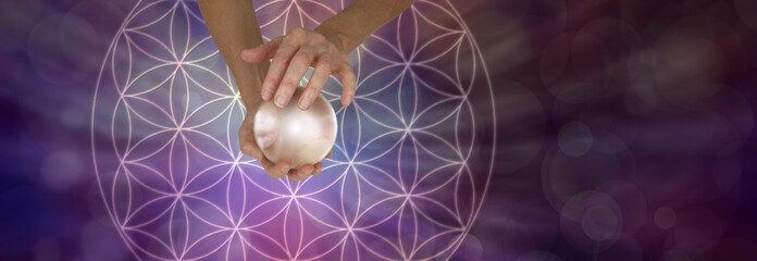 Sacred Geometry and Crystal Ball Scrying - Female holding a large crystal ball above a Flower of Life Symbol on a wide purple bokeh background with copy space
