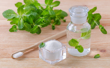 alternative natural mouthwash bottle with toothpaste xylitol, soda, salt, and wood toothbrush closeup, mint on wooden