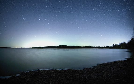 Peaceful night scene with starry sky at a lake in Finland. Reflection of stars on the still water of the lake.