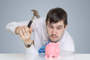 Young man is breaking piggy money bank with hammer to take his savings.