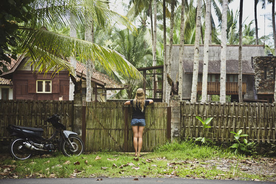 Indonesia, Java, back view of woman leaning on garden gate looking at houses