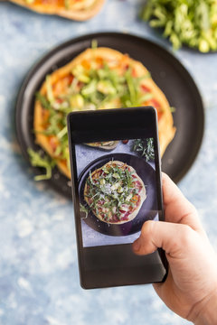 Hand of girl taking picture of homemade vegetarian pizza with cell phone, close-up