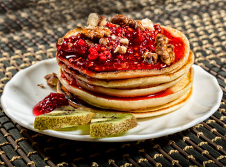Homemade sweet pancakes with raspberry jam on a white plate. Breakfast with stack topped blueberry jam, walnuts and kiwi