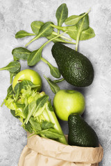 Various green vegetables and fruit - celery, apples, avocado, spinach in a paper package on a light background. Top view. Food background.