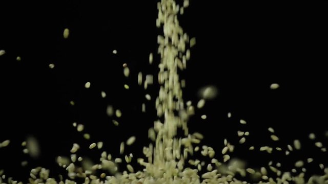 Unprocessed raw is not ground rice pours down on a black background slow mo
