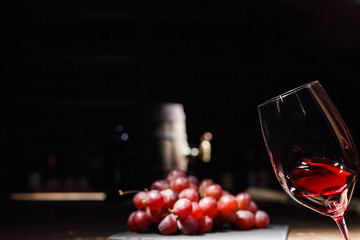 Woman holds glass of wine before bunch of grape lying on black plate
