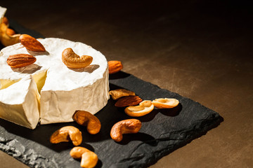 Different kinds of nuts lie on brie cheese on black dish