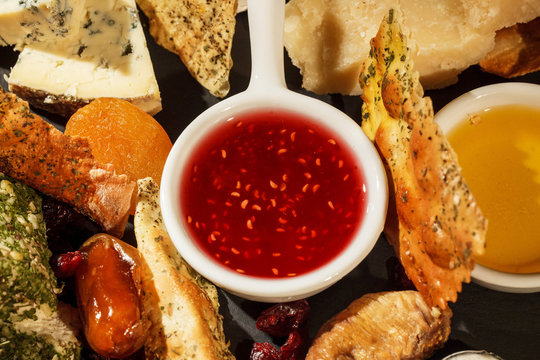 Look From Above At Bowl With Cranberry Sauce Standing Between Pieces Of Cheese On Black Plate