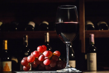 Glass with red wine stands on plate with large grape bunch