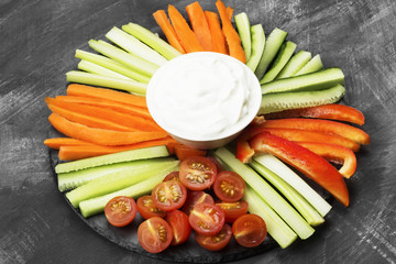 Creamy sauce in white bowl and various vegetables (tomatoes, a celery, cucumbers, carrots) on a dark background. Toning